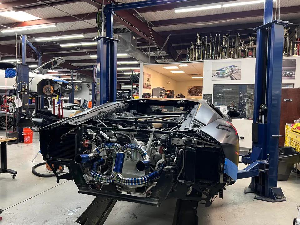 Lamborghini supercar undergoing a turbo kit installation in a performance tuning shop, with the engine bay exposed on a car lift.