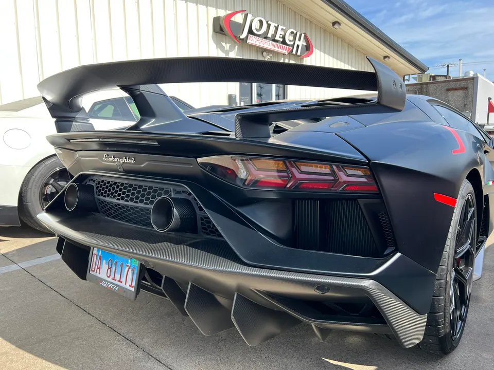 Matte black Lamborghini Aventador SVJ rear view showcasing its large carbon fiber wing and aggressive diffuser outside Jotech Motorsports.