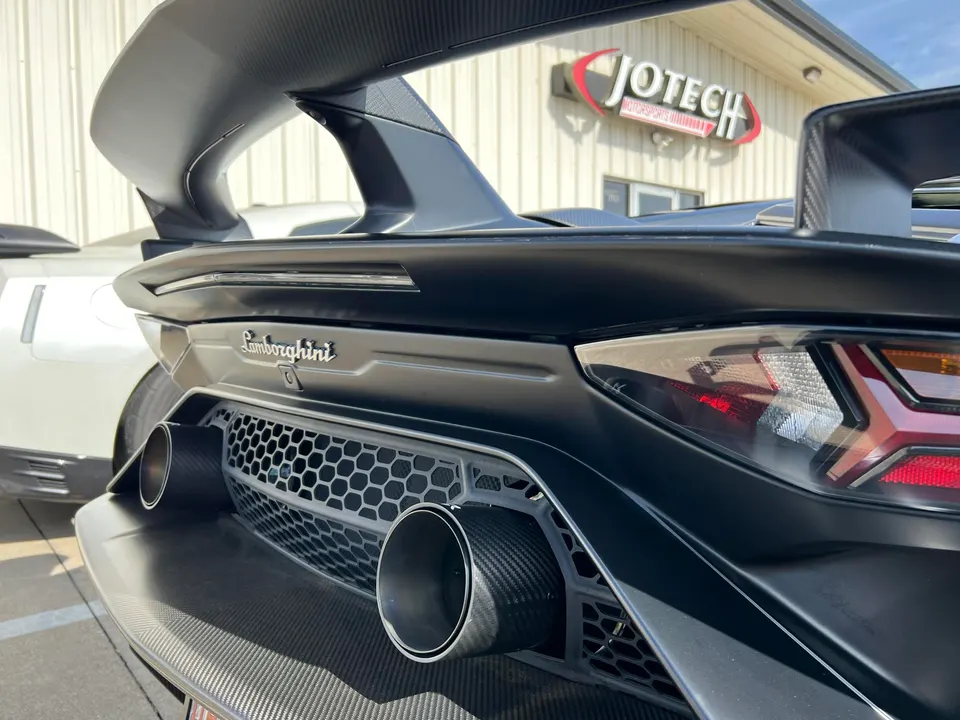 Rear view of a matte black Lamborghini with a carbon fiber rear wing and performance exhaust tips at Jotech Motorsports.