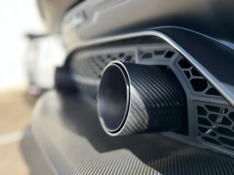 Close-up of a carbon fiber exhaust tip integrated into a car's rear bumper with a honeycomb grille.
