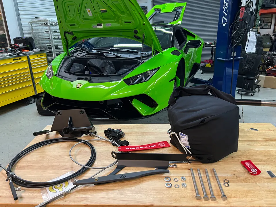 Green Lamborghini Huracan in a Jotech Motorsports shop with drag racing parachute and mounting hardware on a workbench.