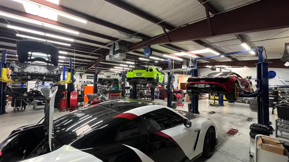 A busy performance tuning shop with multiple high-performance cars, including Nissan GT-Rs and a McLaren, on lifts.