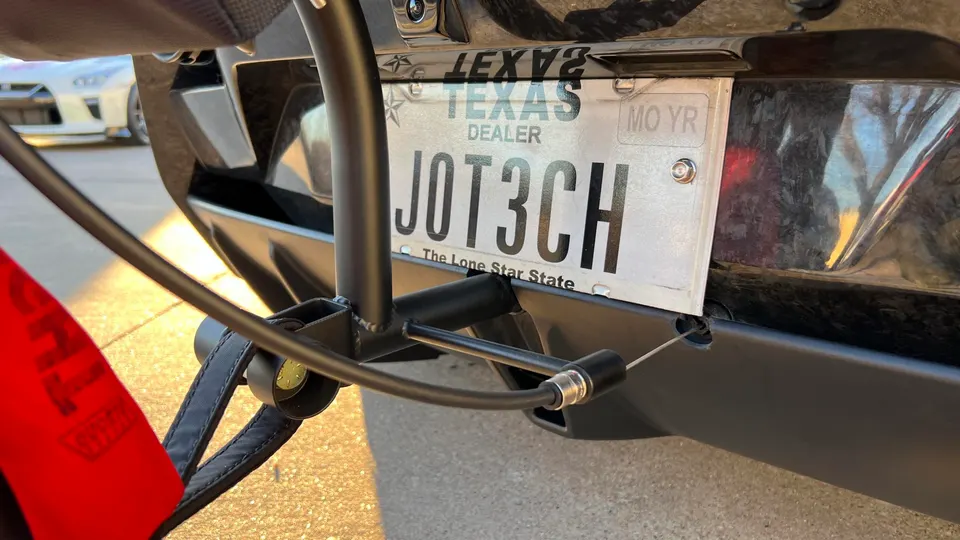 A close-up of a car's rear bumper with a Texas dealer license plate and a bike rack attachment.