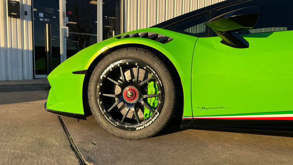 Close-up of a lime green Lamborghini Huracan Performante's front wheel, featuring black Forgeline wheels and green brake calipers.