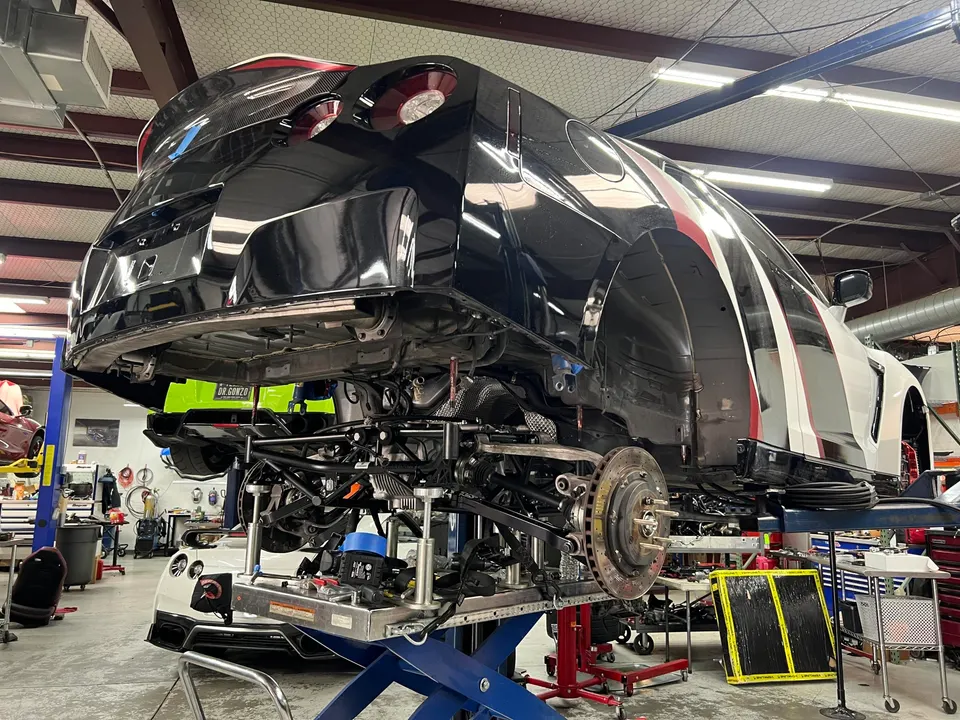 A Nissan GT-R on a lift in a shop, undergoing chassis and suspension work with the body separated.