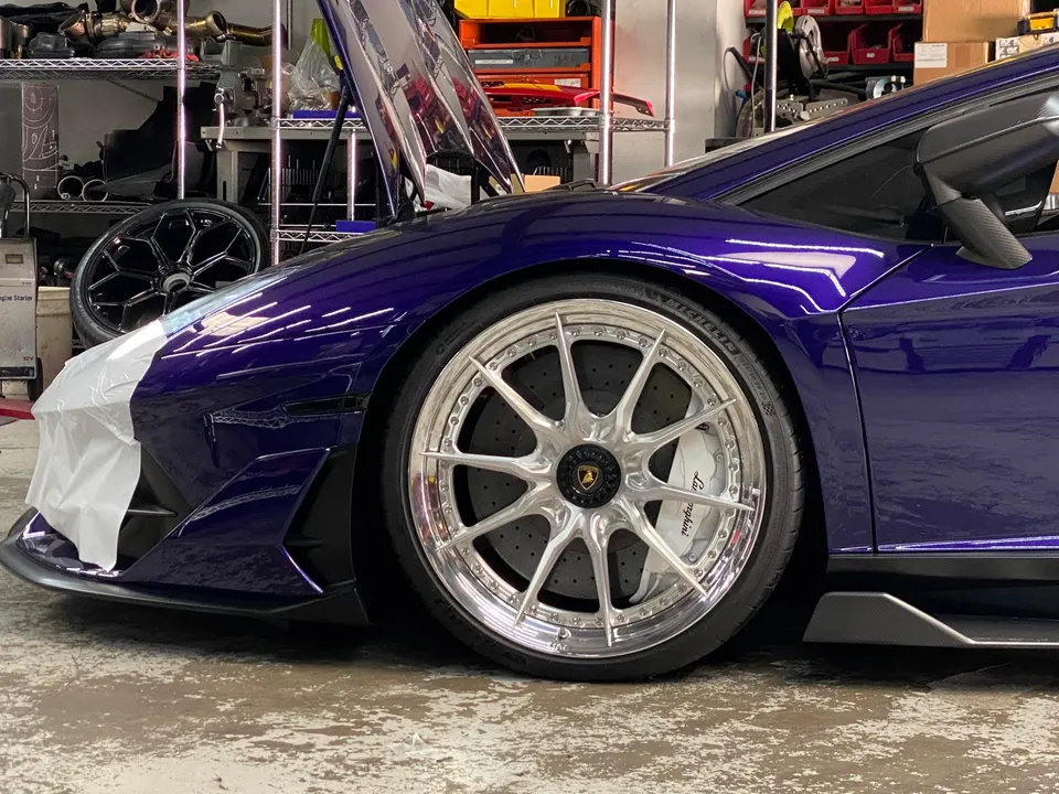 Purple Lamborghini Huracan in a shop with custom aftermarket wheels and performance brakes visible.