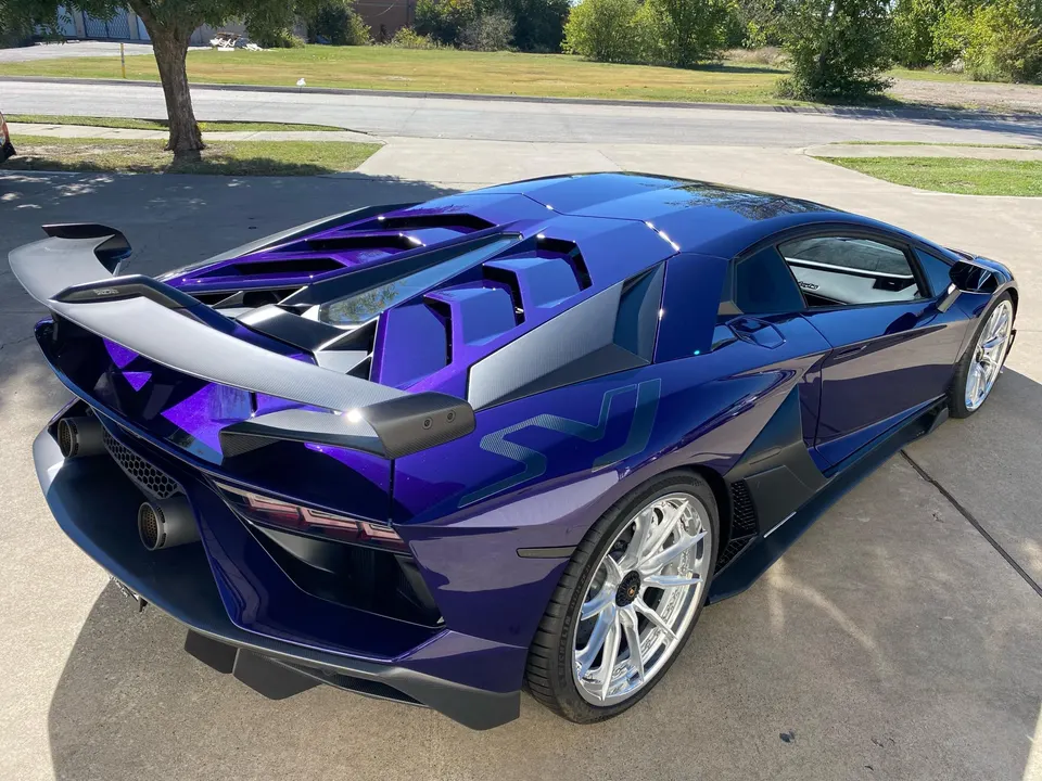 Purple Lamborghini Aventador SVJ with custom wheels and a large carbon fiber rear wing parked outdoors on a sunny day