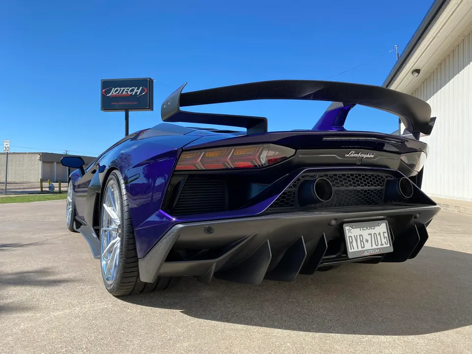A purple Lamborghini Aventador with a large carbon fiber wing and rear diffuser parked outside Jotech Motorsports.