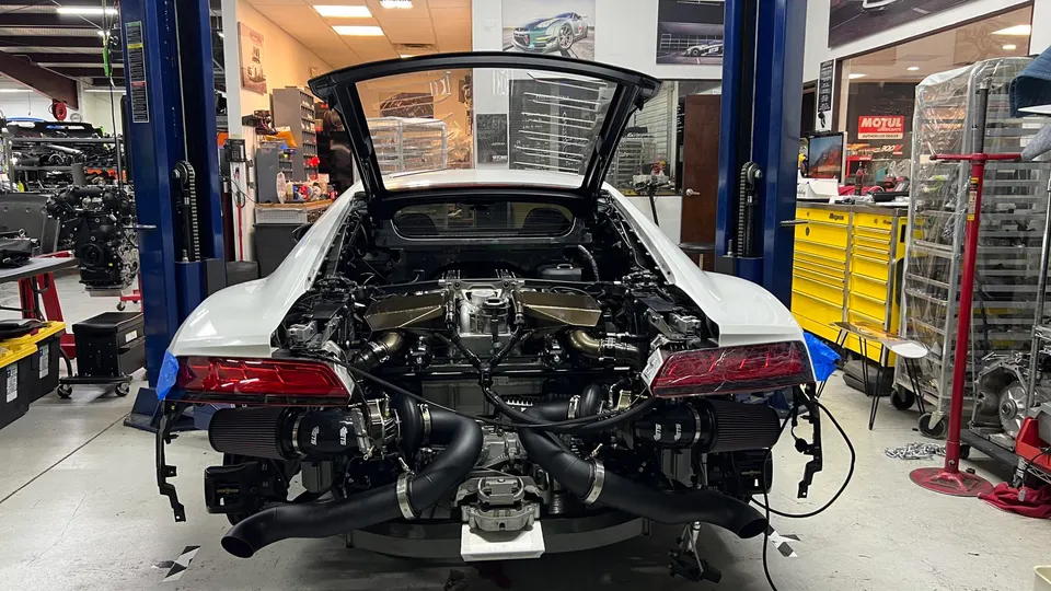 Rear view of a white Audi R8 on a lift in a performance shop, showcasing a twin-turbo engine build.