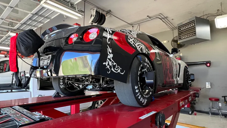 A black and white custom Nissan GT-R drag car on an alignment rack in a performance tuning shop.