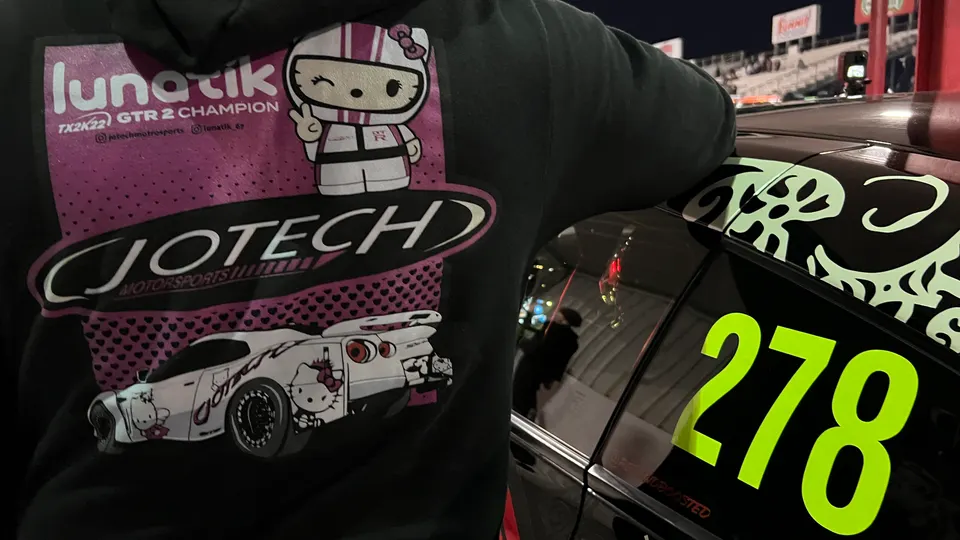 A person wearing a Jotech Motorsports Hello Kitty race car hoodie at a drag strip, with a black race car number 278 visible.