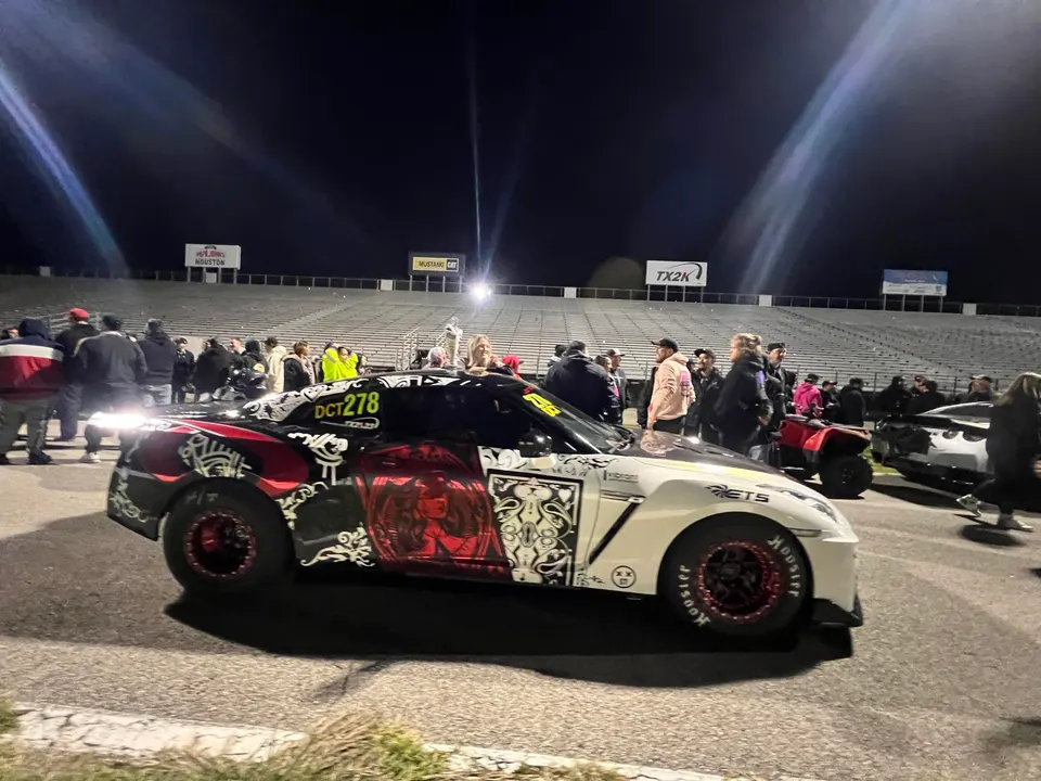 A highly modified Nissan GT-R drag car with a custom red and white wrap in a staging lane at a night drag race event.
