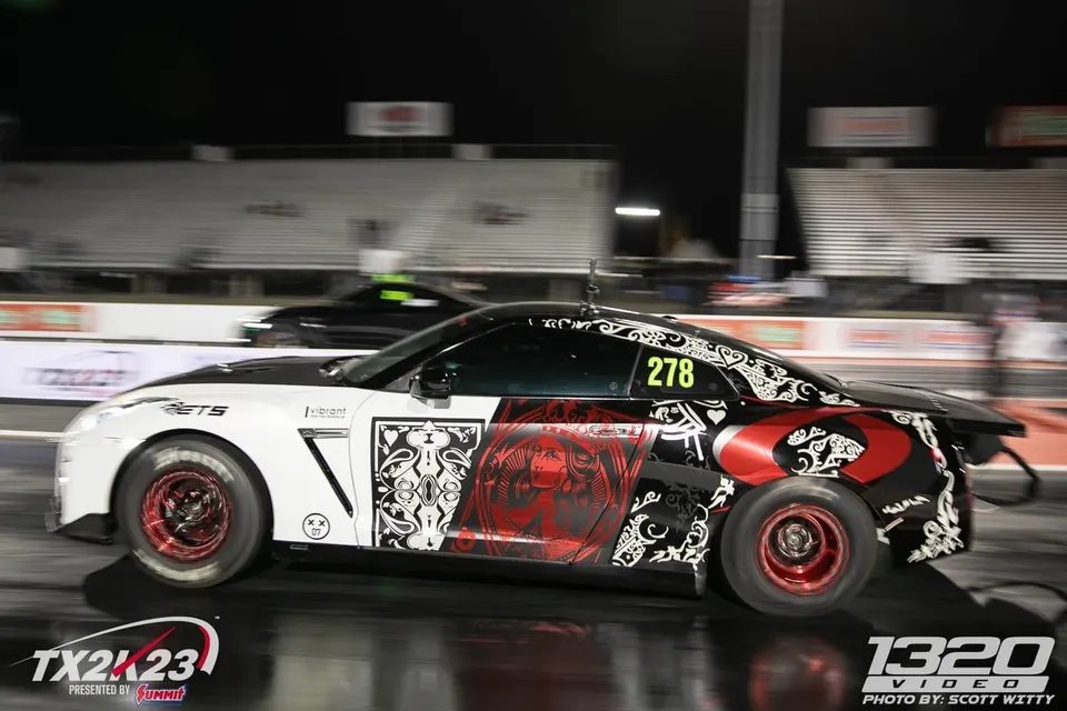 A custom-liveried Nissan GT-R drag racing at night during TX2K23, with another car in the background.