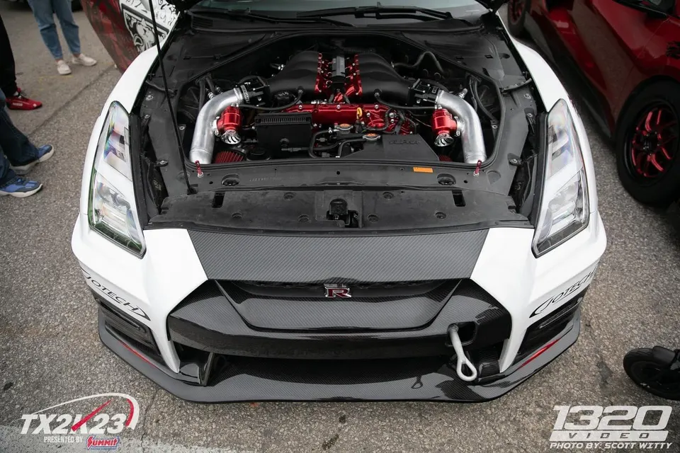 Front view of a white Nissan GT-R R35 with its hood open, showcasing a highly modified red and silver engine bay with carbon fiber accents.
