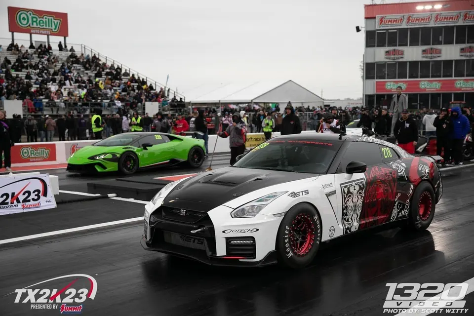 Two high-performance cars, a white and black Nissan GT-R and a green Lamborghini Huracan, at the TX2K23 drag strip.