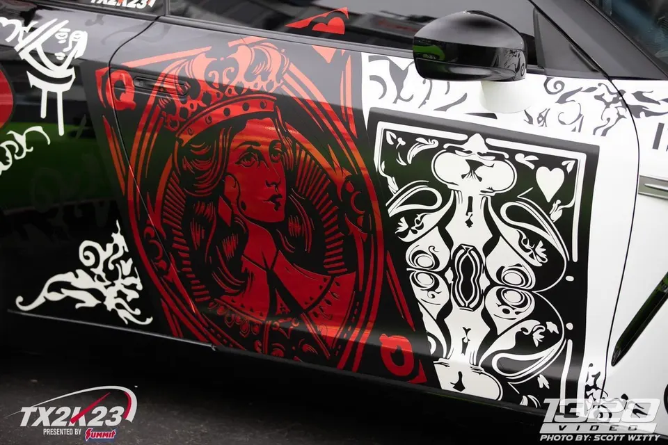 Close-up of a car's side featuring a custom red and black playing card wrap with a queen of hearts design.