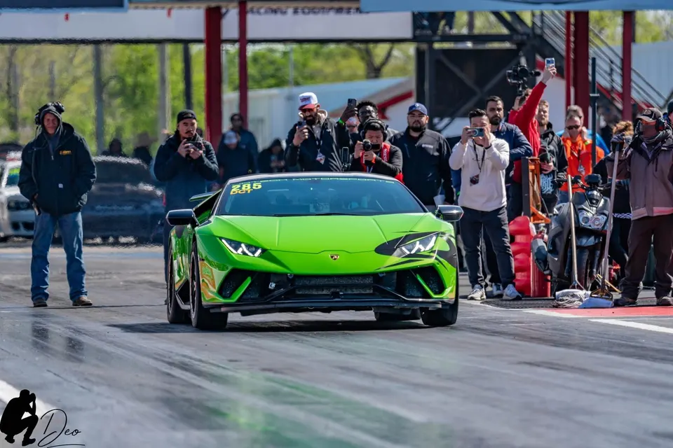 A vibrant green Lamborghini Huracan race car at the starting line of a drag strip, surrounded by spectators.