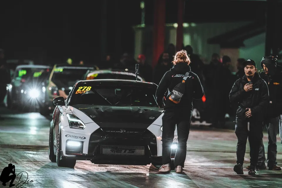 A Jotech-tuned Nissan GT-R in the staging lanes of a drag strip at night, with crew members standing nearby.