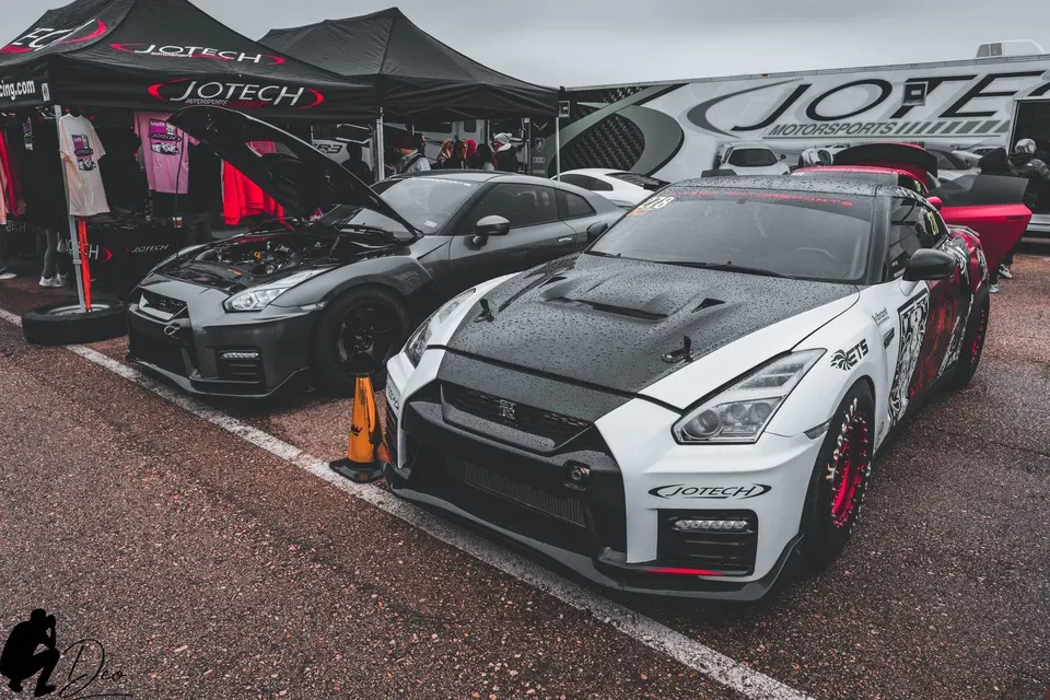Two highly modified Nissan GT-R R35s, one white with a custom wrap and one grey with its hood open, displayed at a Jotech Motorsports event.