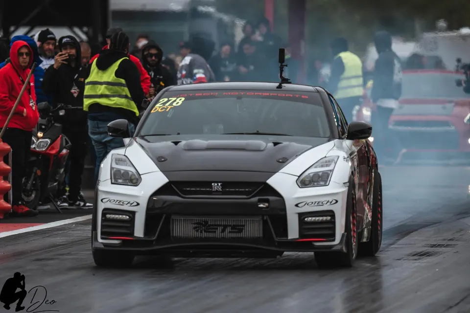 A white and black Nissan GT-R with a large front-mounted intercooler on a drag strip, ready to race, with a Jotech Motorsports banner.