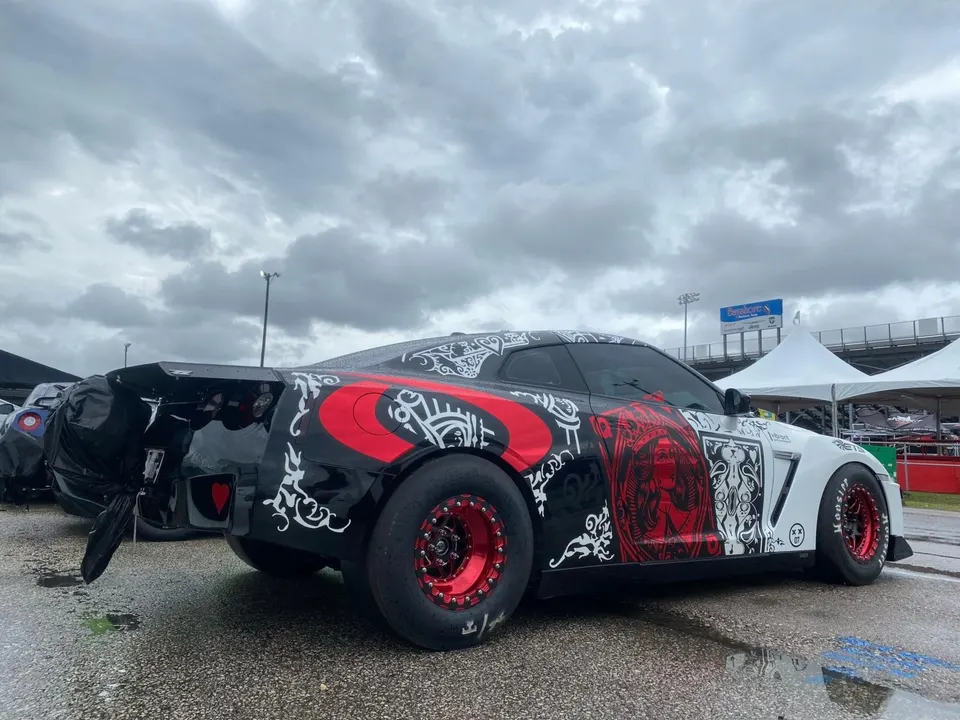 Highly modified Nissan GT-R drag car with custom black and white wrap, red wheels, and a parachute at a track event.
