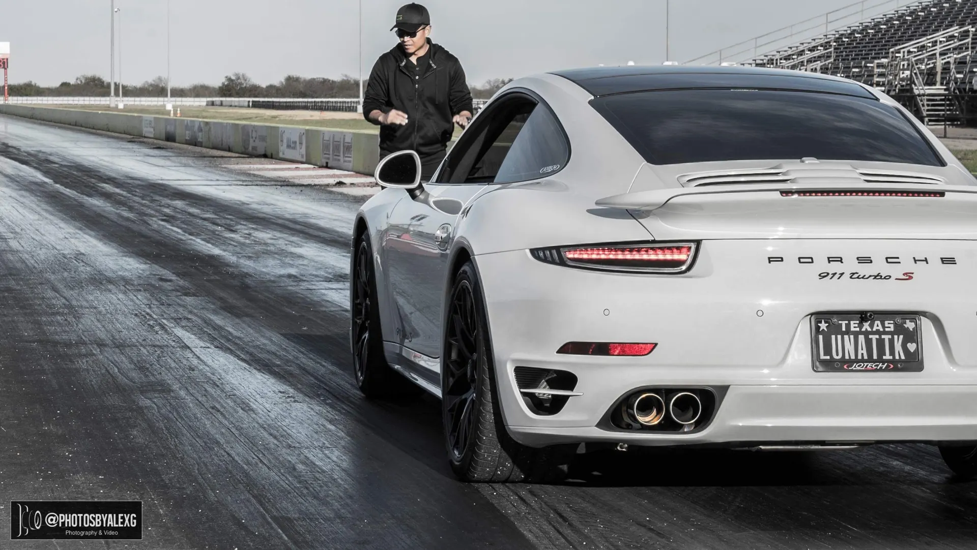White Porsche 911 Turbo S on a drag strip with a person standing next to it, ready for a run.
