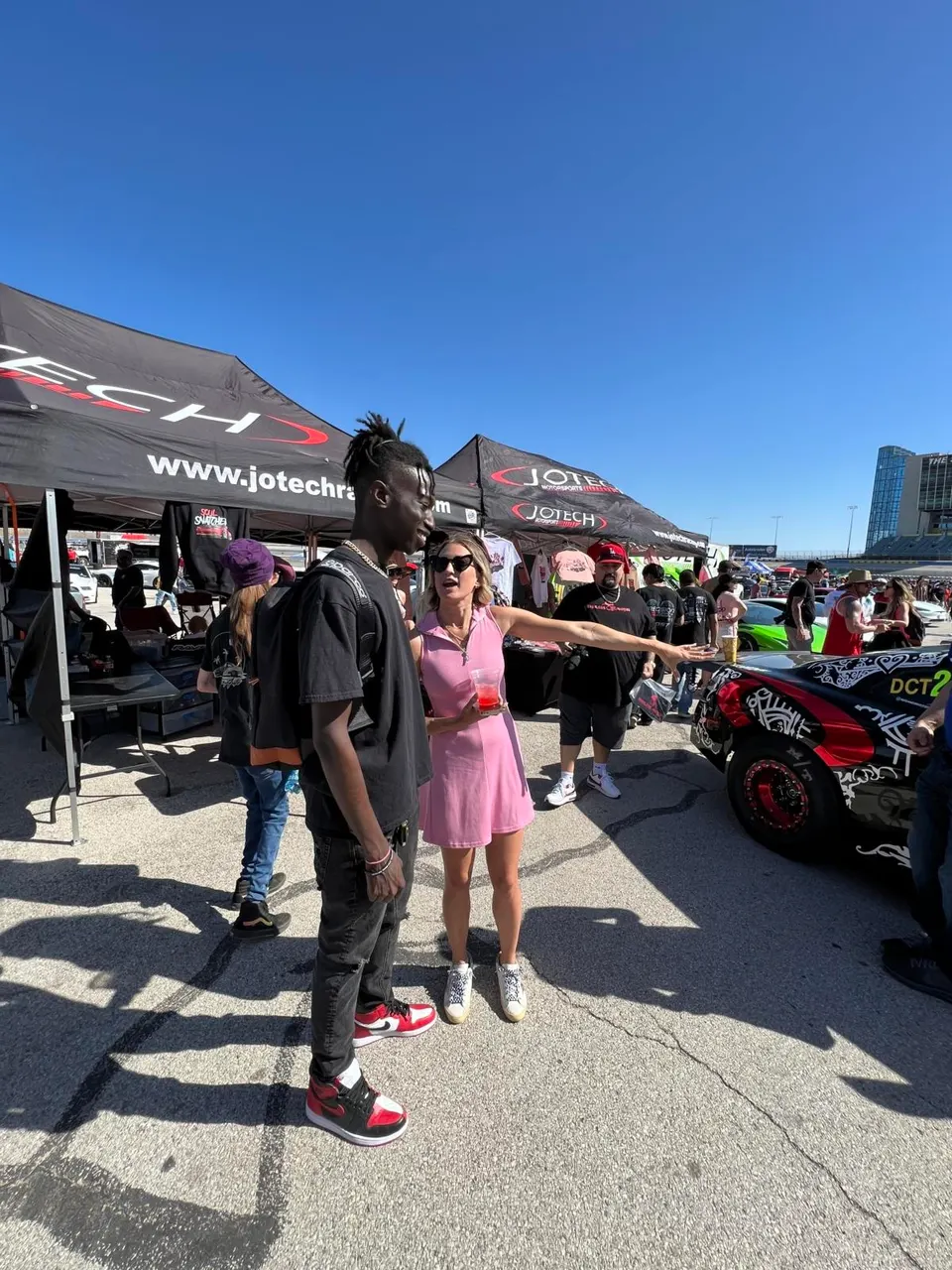 People gather around a custom-wrapped car at the Jotech Motorsports booth during an outdoor car event.