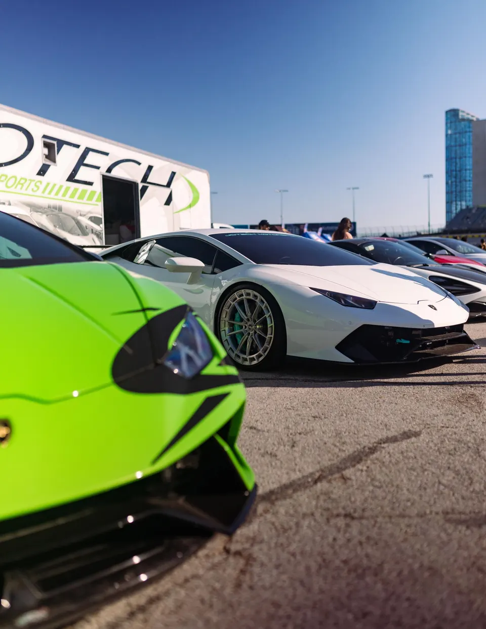 A line of high-performance Lamborghinis, including a white Huracan and a neon green supercar, parked at a Jotech Motorsports event.
