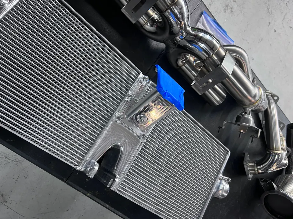 High-performance aluminum intercooler and stainless steel exhaust manifold laid out in a tuning shop.