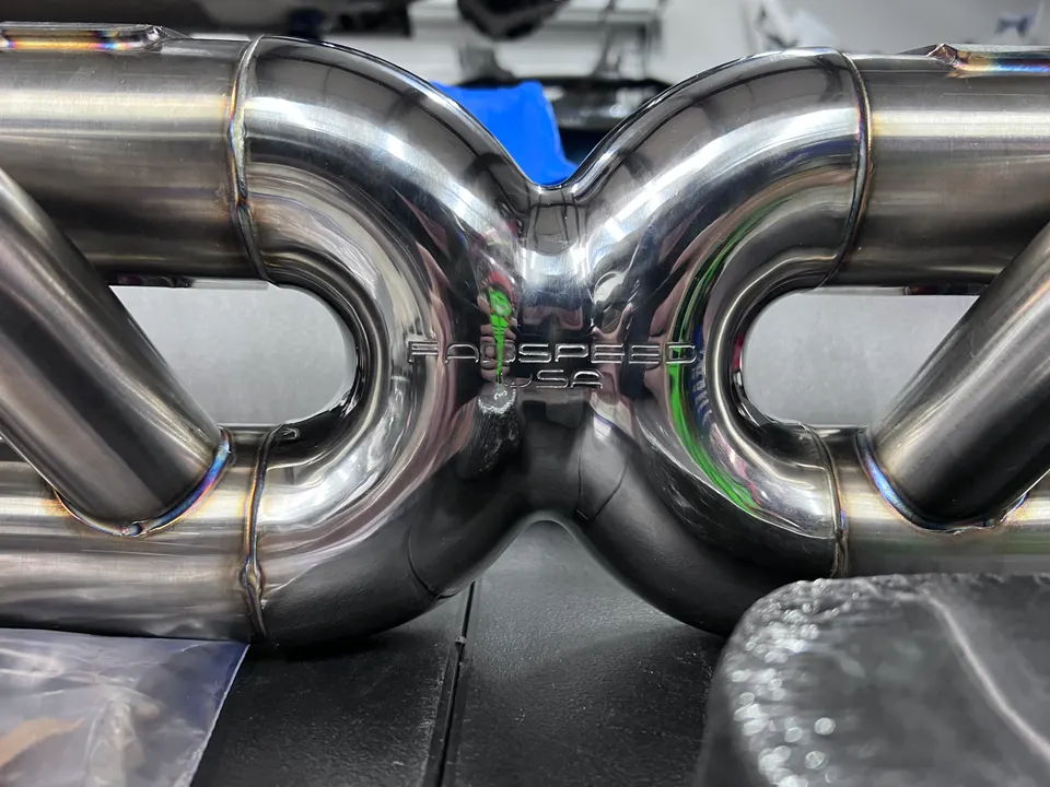 Close-up of a Fabspeed USA stainless steel exhaust component with visible welds and polished finish.
