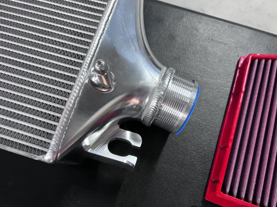 Close-up of an aluminum intercooler and a red performance air filter on a dark surface, showcasing performance parts.