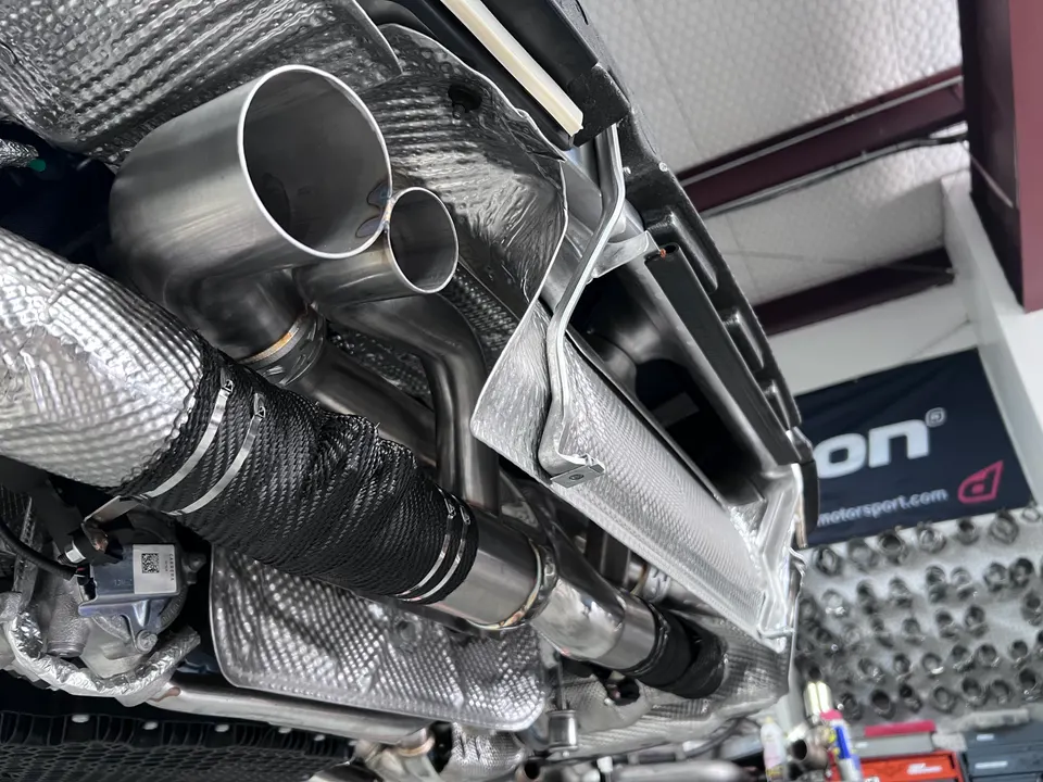 A close-up detail view of a performance exhaust system with heat wrap installed on the underside of a car in a shop.