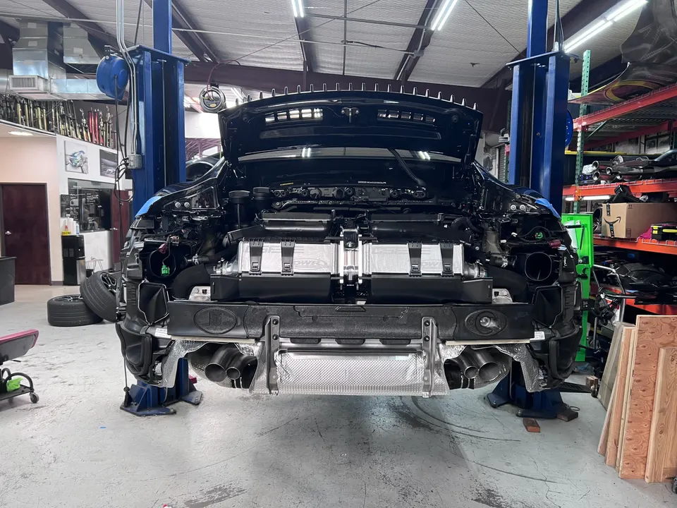 A black Porsche 911 on a lift in a performance shop with the rear bumper removed, showcasing the exhaust and intercoolers.