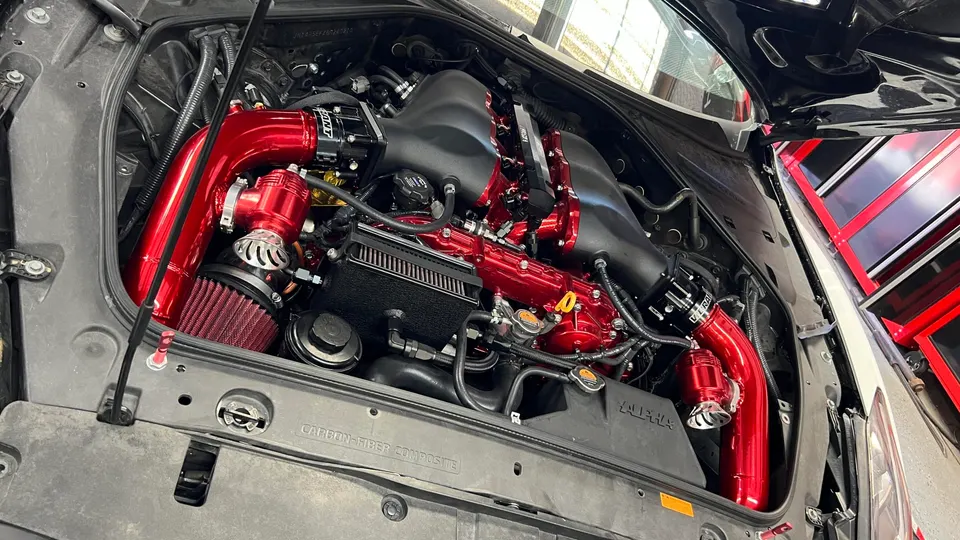 Close-up of a highly modified Nissan GT-R engine bay featuring red aftermarket intake pipes, blow-off valves, and a black intake manifold.