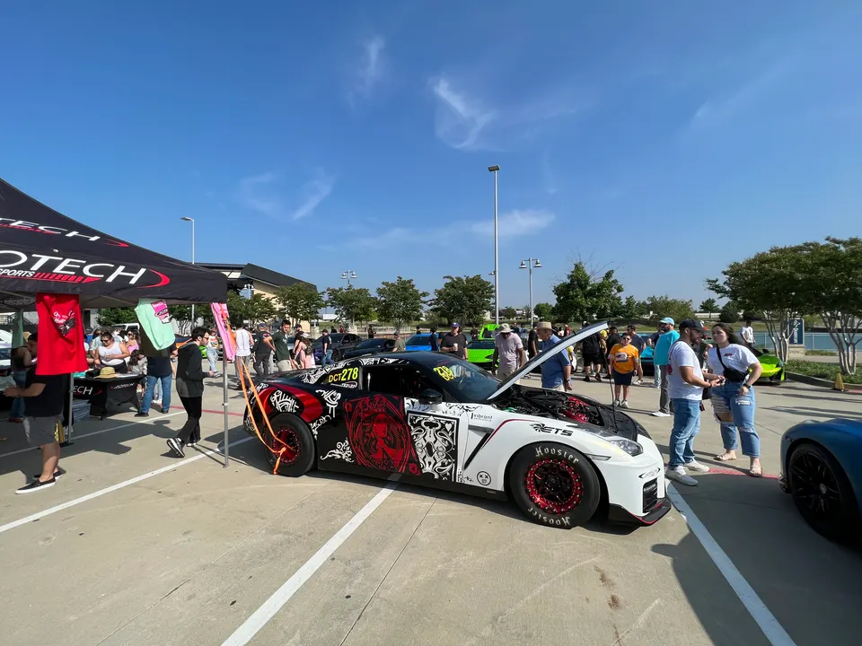 A highly modified Nissan GT-R with its hood open, showcasing the engine, at an outdoor car show with a crowd.