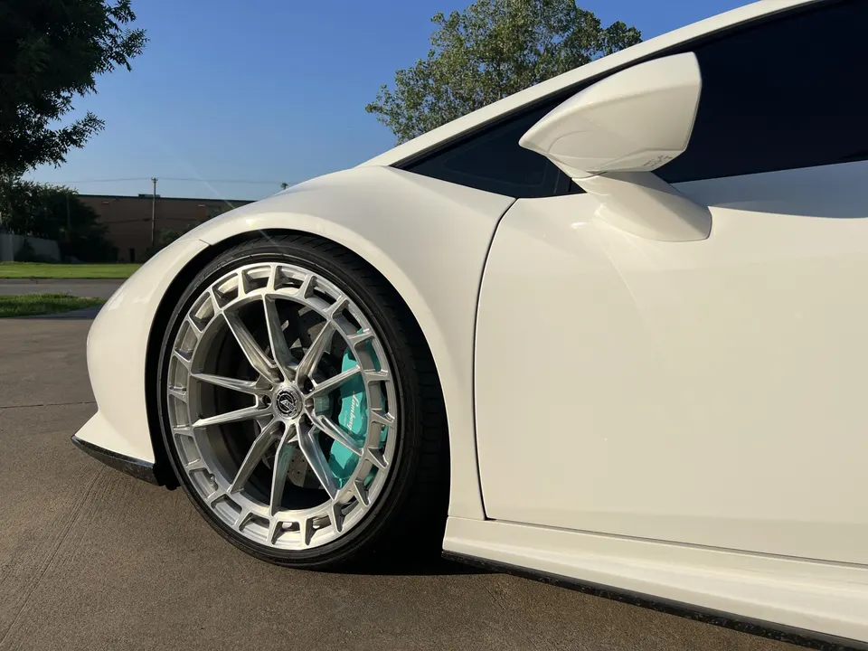 Close-up of a white Lamborghini's custom silver forged wheels and teal brake calipers.