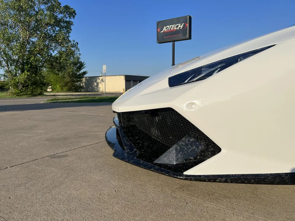 White Lamborghini supercar with a carbon fiber front splitter parked outdoors, with a Jotech sign in the background.