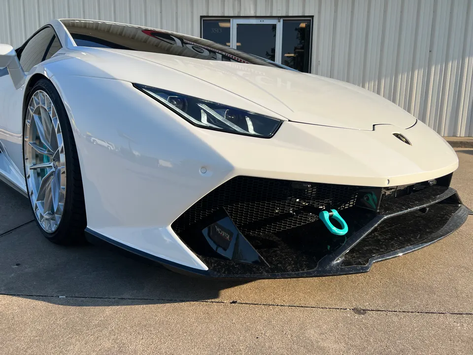 White Lamborghini Huracan with a carbon fiber front splitter and a blue tow hook, showcasing aftermarket wheels.