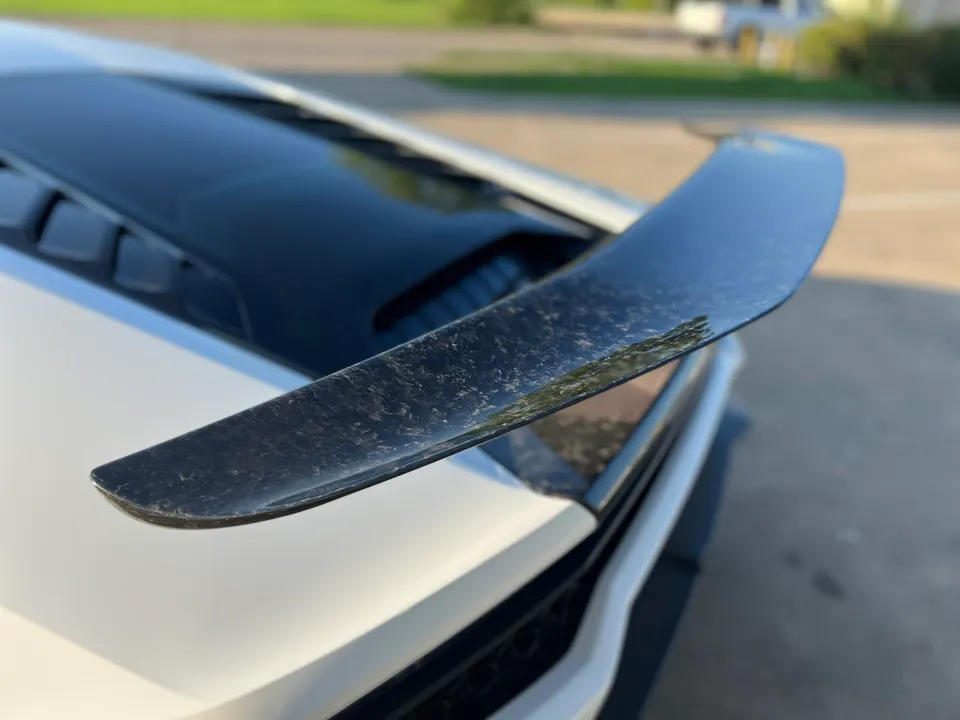 Close-up of a forged carbon fiber rear wing on a white Lamborghini supercar, showcasing the intricate pattern.