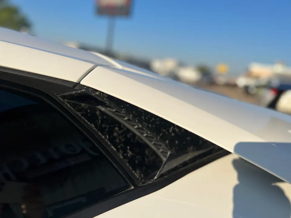 Close-up of a white car's carbon fiber side vent, showcasing exterior aerodynamic detail.