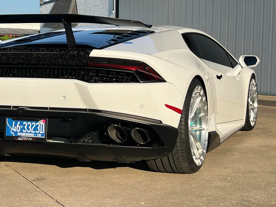 A white Lamborghini Huracan with a large carbon fiber rear wing, aftermarket wheels, and quad exhaust tips.