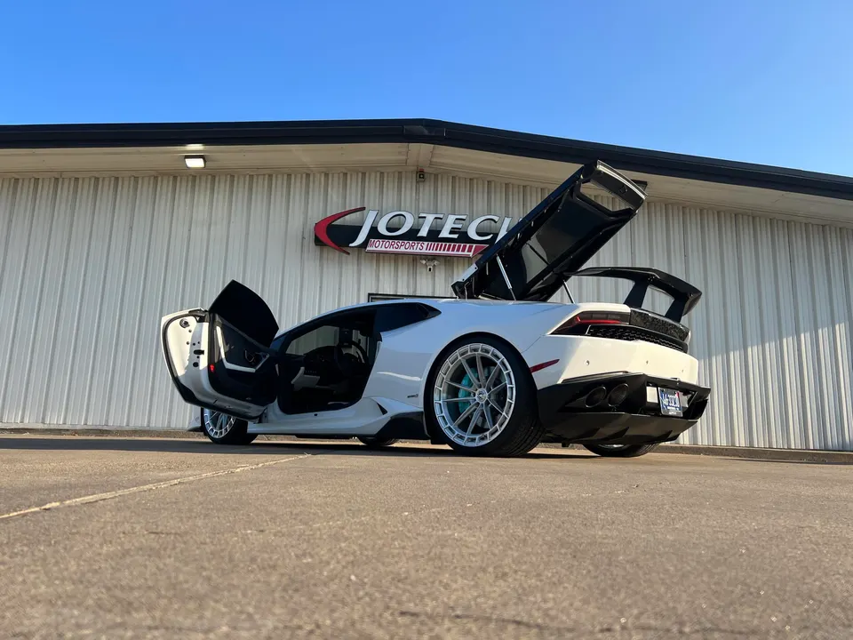 A white Lamborghini Huracan with custom wheels and a large rear wing parked outside Jotech Motorsports.