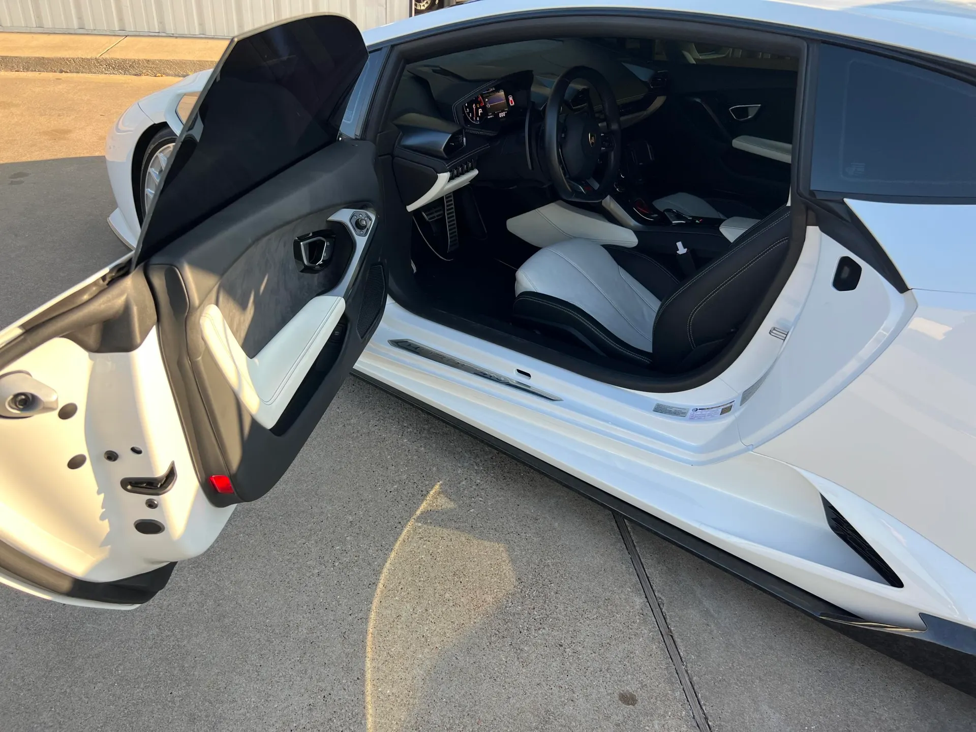 A white Lamborghini Huracan with the driver's door open, showcasing the black and white two-tone interior.