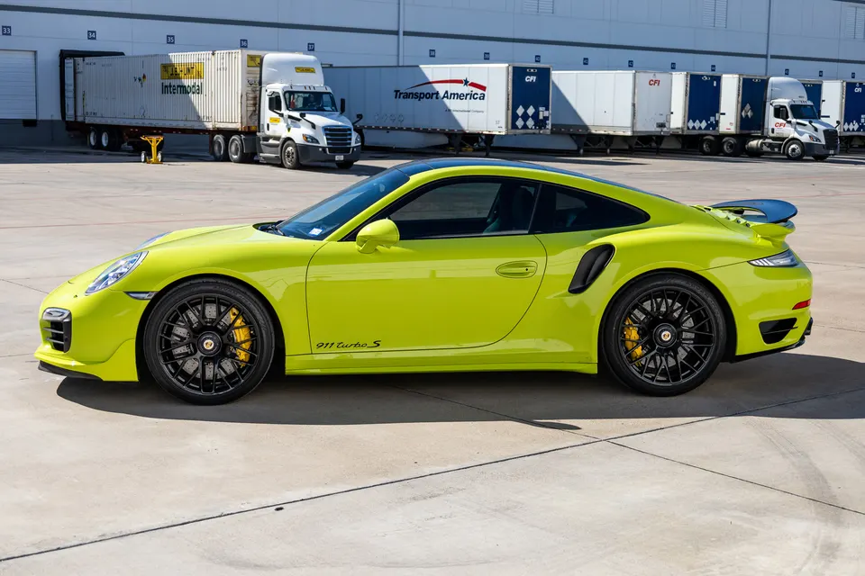 Lime green Porsche 911 Turbo S parked in front of a warehouse with semi-trucks and loading docks.