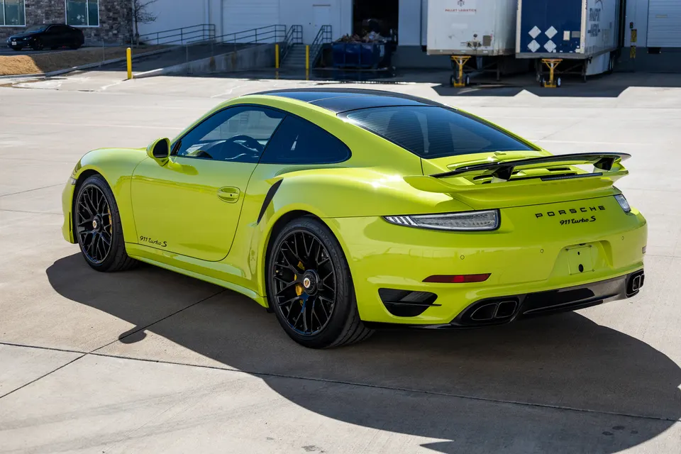 Lime green Porsche 911 Turbo S with black aftermarket wheels and a rear wing parked in a lot.