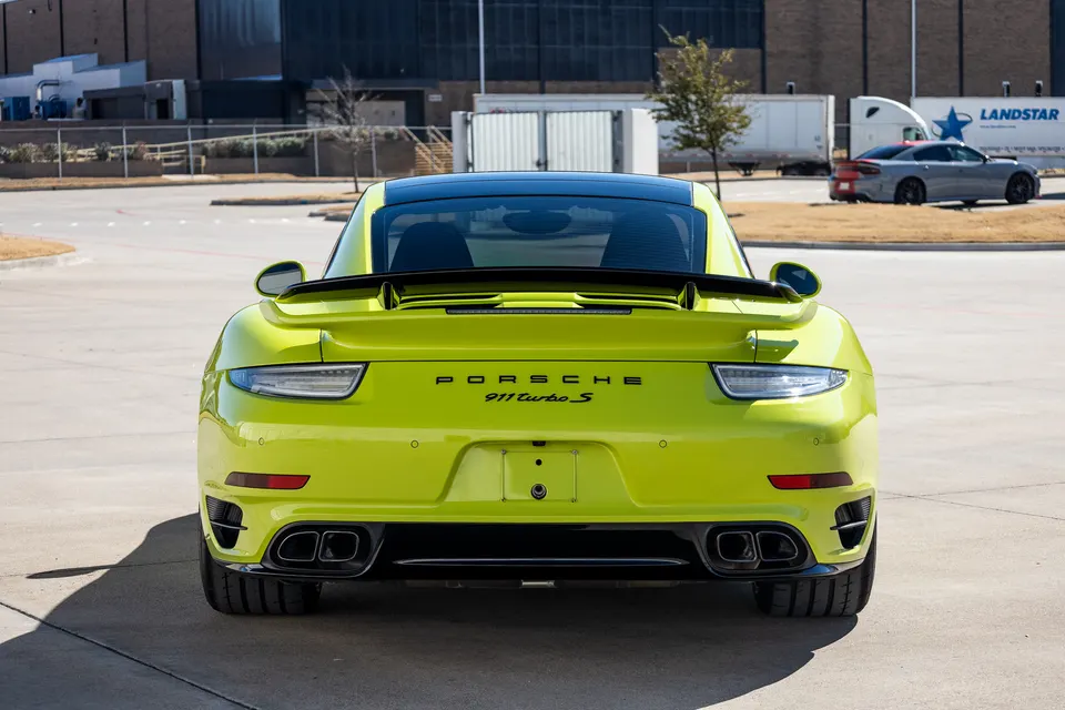 A lime green Porsche 911 Turbo S from the rear, showcasing its distinctive tail lights, quad exhaust tips, and rear wing.