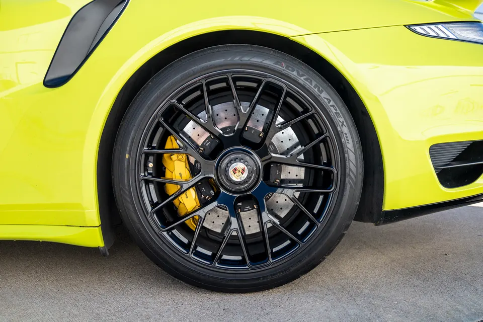 Close-up of a vibrant yellow Porsche's front wheel, featuring black multi-spoke wheels and bright yellow brake calipers.
