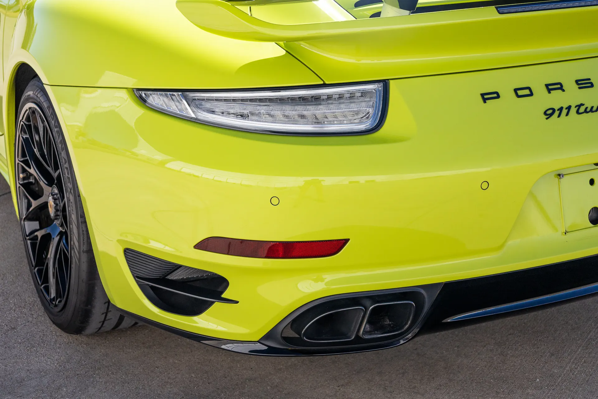 Rear view of a bright yellow Porsche 911 Turbo, showcasing its taillight, bumper, and dual exhaust tips.