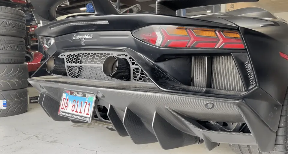 Rear view of a black Lamborghini with a large carbon fiber diffuser, central exhaust, and LED taillights in a shop.