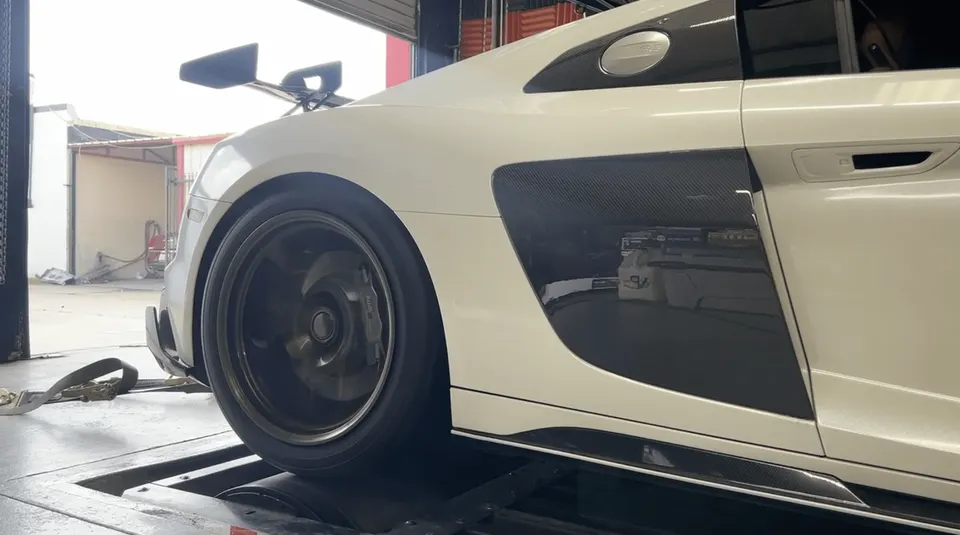White Audi R8 supercar on a dynamometer for performance testing, showing the rear wheel and carbon fiber side blade.